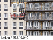 ANGARSK, IRKUTSK REGION, RUSSIA - October 08, 2024: Builders install facade tiles on wall of high-rise residential building from suspended construction cradle. Сoncept of improving lives of city dwellers. Редакционное фото, фотограф Виктория Катьянова / Фотобанк Лори