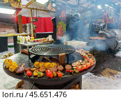 Holiday fair on the street in winter in the city. Cooking vegetables on the grill at the festivities (2024 год). Редакционное фото, фотограф Zima Nadezhda / Фотобанк Лори