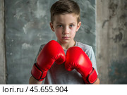 A boy in boxing gloves strikes, a cute teenage boy stands in a fighter's pose, ready to fight. Playing sports. Children's sports sections. Стоковое AI-изображение, AI-художник Photojuli / Фотобанк Лори