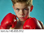 A boy in boxing gloves strikes, a cute teenage boy stands in a fighter's pose, ready to fight. Playing sports. Children's sports sections. Стоковое AI-изображение, AI-художник Photojuli / Фотобанк Лори
