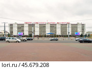 Типовое жилое здание на центральной улице Ленина с лозунгом о подвиге советского народа в городе Витебске, Белоруссия. Здание с яркими экранами и облачное небо создают атмосферу исторической значимости. По улице проезжают современные иностранные автомобили, символизируя контраст смыслов. Редакционное фото, фотограф Сергей Никифоров-Гордеев / Фотобанк Лори