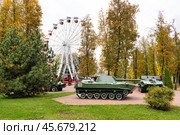 Современная военная техника, бронетранспортеры в городском зеленом парке Витебска на фоне колеса обозрения. Символ былых и настоящих побед на врагами и памяти о защитниках страны. Осенние деревья создают атмосферу спокойствия и ностальгии. Редакционное фото, фотограф Сергей Никифоров-Гордеев / Фотобанк Лори