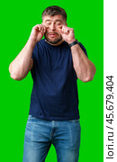 Man expressing frustration with tired eyes while standing in front of a bright green background. Стоковое фото, фотограф Сергей Толмачёв / Фотобанк Лори
