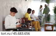 Relaxed young guy browsing websites on smartphone while sitting in lobby of job center or employment office, waiting for interview or conversation with career counselor. Стоковое видео, видеограф Яков Филимонов / Фотобанк Лори