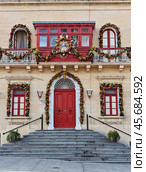 Close-Up of Historic Building with Red Door and Festive Christmas Garlands in Malta. Стоковое фото, фотограф Kira_Yan / Фотобанк Лори