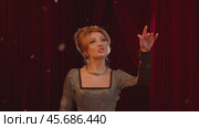 Actress performs on stage of theater with backdrop of red curtain. During performance, snow gently falls around her, adding to atmosphere. Стоковое видео, видеограф Strunov David / Фотобанк Лори