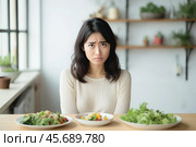 Young woman choosing between different salads at home, showing disgust and indecision. Стоковое AI-изображение, AI-художник Иван Рябоконь / Фотобанк Лори