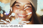 Smiling Girl with Fire Sparkler Glow in the Winter Season. pleased happy smiling young 20s woman is holding a bright sparkler in a festive winter setting. Glowing blur bokeh light on background. Стоковое AI-видео, аниматор Марина Демидюк / Фотобанк Лори