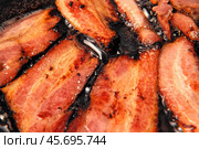 Frying Bacon Slices in a Pan. Crispy Pieces of Delicious Red Thin Smokey Bacon Fried in a Hot Skillet. Traditional Breakfast. Smoked Bacon Rasher or Strip Being Cooked. Grill. Fat High Calorie Food. Стоковое фото, фотограф Марина Демидюк / Фотобанк Лори