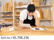Bakery guy employee in apron examines documents, ponders debt restructuring. Стоковое фото, фотограф Яков Филимонов / Фотобанк Лори