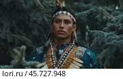 A young man dressed in traditional attire stands confidently among the trees, showcasing Indian American and Native American heritage. Стоковое AI-видео, аниматор Ксения Лаптева / Фотобанк Лори