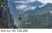 Mountain cable car. The cabins of the funicular on a rope over the abyss. Green vegetation on the steep slopes of the cliffs. Peaks in the clouds. China. Tianmen Mountain. Hunan. Стоковое фото, фотограф Вера Ивановна Кубарева / Фотобанк Лори