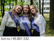 Three happy graduates wearing sashes stand together in a park, celebrating their last day of school with pride and excitement for the future. Стоковое фото, фотограф Mikhail Davidovich / Фотобанк Лори