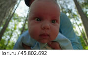 A bearded man tilts a baby in a blue onesie towards the camera until the baby's face takes up the entire frame. Sunlit forest in the background. Father and son in nature. Стоковое видео, видеограф Воловодов Владимир / Фотобанк Лори