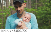 A bearded man in a black baseball cap and blue jersey carries an infant in his arms in a pine forest. Front view. Father and son walking in a park on a summer day. Close-up. Стоковое видео, видеограф Воловодов Владимир / Фотобанк Лори