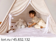 Happy little caucasian boy is lying in a wigwam. Childhood, playing with soft toys, tenderness. Children's room with a teepee tent. Cozy atmosphere interior of a children's room. Стоковое фото, фотограф Ирина Михайличенко / Фотобанк Лори