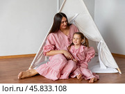 Happy overjoyed mother and her little daughter, little girl in pink pajamas sitting in children hut tent at home and have fun together. Children room. Copy space. Стоковое фото, фотограф Ирина Михайличенко / Фотобанк Лори