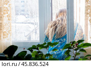 Woman with long blonde hair stands near an open window and looks out into the street. Стоковое фото, фотограф Коханова Наталья / Фотобанк Лори