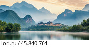 Picturesque xingping fishing village reflecting in li river at sunrise with misty karst mountains in background. Стоковое AI-изображение, AI-художник Юрий Поздников / Фотобанк Лори
