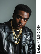 Rapper wearing gold chains and black leather jacket posing in studio. Стоковое AI-изображение, AI-художник Юрий Поздников / Фотобанк Лори