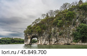 A picturesque rock by the river bank. Round arched opening above the water. Green vegetation on steep rocky slopes. A stone tower against a cloudy sky. China. Elephant Trunk Hill. Xiangbishan. Guilin. Стоковое фото, фотограф Вера Ивановна Кубарева / Фотобанк Лори