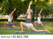 Elderly woman performing Anjaneyasana during group yoga training in park. Стоковое фото, фотограф Яков Филимонов / Фотобанк Лори