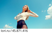 Fashionable woman posing under bright blue sky, wearing beige long-sleeve top and black tights, confident expression, minimal outdoor background, sunny weather, modern style, fresh look. Стоковое AI-изображение, AI-художник Павел Муравьев / Фотобанк Лори
