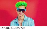 Young man with dyed hair and sunglasses posing on red background. Стоковое видео, видеограф Данил Руденко / Фотобанк Лори