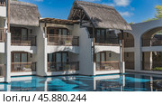 The thatched-roof hotel building is located directly by the swimming pool. Terraces with latticed railings over blue water. Reflection. Azure sky, clouds. Mauritius. Belle Mare. Стоковое фото, фотограф Вера Ивановна Кубарева / Фотобанк Лори
