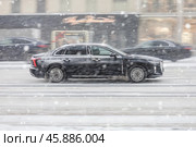 Side view rolling shot in black color sedan car in motion. Hongqi H5 driving along winter street in city during blizzard. Редакционное фото, фотограф Константин Григорьев / Фотобанк Лори