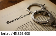 Close-up of handcuffs on book page titled financial crimes, representing legal problems, fraud, corruption, white-collar crime, justice, financial sector. Стоковое AI-изображение, AI-художник Павел Муравьев / Фотобанк Лори