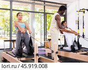 Girl doing pilates exercises with reformer bed in studio. Active lifestyle and fitness concept. Стоковое фото, фотограф Яков Филимонов / Фотобанк Лори