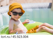 It's a hot day. A cute boy in sunglasses and a panama hat swims on a circle in a foam pool. The concept of summer holidays with children. Стоковое фото, фотограф Photojuli / Фотобанк Лори