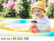 It's a hot summer day. Cute boy swims in the pool. The child drinks refreshing lemonade. The concept of summer holidays with children and refreshing drinks. Стоковое фото, фотограф Photojuli / Фотобанк Лори