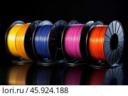 Colorful filament spools for 3d printing resting on black surface. Стоковое AI-изображение, AI-художник Иван Рябоконь / Фотобанк Лори