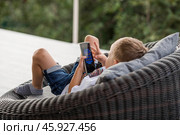 A 5-year-old little boy with a smartphone in his hands on the veranda. The child is playing on the phone. Harm of gadgets for children. Protect your child from the smartphone. Kids and gadgets. Стоковое фото, фотограф Photojuli / Фотобанк Лори