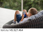A 5-year-old little boy with a smartphone in his hands on the veranda. The child is playing on the phone. Harm of gadgets for children. Protect your child from the smartphone. Kids and gadgets. Стоковое фото, фотограф Photojuli / Фотобанк Лори