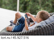 A 5-year-old little boy with a smartphone in his hands on the veranda. The child is playing on the phone. Harm of gadgets for children. Protect your child from the smartphone. Kids and gadgets. Стоковое фото, фотограф Photojuli / Фотобанк Лори