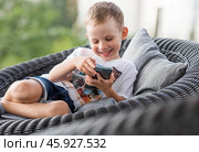 A 5-year-old little boy with a smartphone in his hands on the veranda. The child is playing on the phone. Harm of gadgets for children. Protect your child from the smartphone. Kids and gadgets. Стоковое фото, фотограф Photojuli / Фотобанк Лори