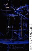 Close-up of a drum kit and a drummer behind it on a dark stage with blue lighting. The background is blurred. Стоковое фото, фотограф Воловодов Владимир / Фотобанк Лори
