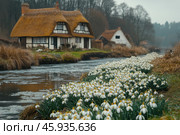 Beautiful blooms of spring snowdrops, Galanthus nivalis, by the side of the river that runs through the village with thatched cottages in the background. Стоковое AI-изображение, AI-художник Ирина Михайличенко / Фотобанк Лори