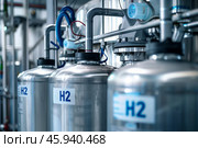 A row of silver tanks labeled with H2, indicating hydrogen storage, in a modern industrial facility. Стоковое AI-изображение, AI-художник Михаил Строгалев / Фотобанк Лори