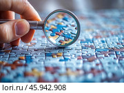 The process of assembling a puzzle. A close-up of a person's hand holding a magnifying glass allows the details of one of the puzzle pieces to be seen with greater clarity. The surface of the table is littered with assembled puzzle pieces, forming a multi-colored image. The colors of the puzzle include shades of blue, orange, and brown, creating an atmosphere of concentration and attention to detail. Light falls softly on the surface, emphasizing the texture of the puzzle pieces. The image symbolizes care, meticulousness, and pleasure from the assembly process. Стоковое AI-изображение, AI-художник Анна Кривицкая / Фотобанк Лори