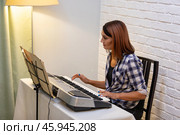Beautiful woman in checkered shirt playing music synthesizer at home, composes music, learns musical scores. Стоковое фото, фотограф Ольга Яковенко / Фотобанк Лори