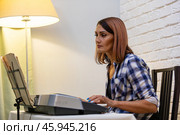 Beautiful woman in checkered shirt playing music synthesizer at home, composes music, learns musical scores. Стоковое фото, фотограф Ольга Яковенко / Фотобанк Лори