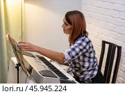 Beautiful woman in checkered shirt playing music synthesizer at home, composes music, learns musical scores. Стоковое фото, фотограф Ольга Яковенко / Фотобанк Лори