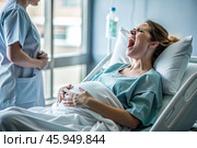 A pregnant woman in a hospital bed in the maternity ward. The woman is in labor and screaming in pain. Pregnancy and childbirth. Стоковое AI-изображение, AI-художник Photojuli / Фотобанк Лори