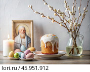 Orthodox Easter. Easter cake, painted eggs, icon, faces of saints, willow in a vase, church candles and Easter decor on a wooden table in an old village house. Стоковое AI-изображение, AI-художник Photojuli / Фотобанк Лори