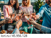 Glasses of pink sparkling wine in the hands of people. People are relaxing on the outdoor veranda. The concept of recreation, corporate event, party or celebration. Стоковое AI-изображение, AI-художник Photojuli / Фотобанк Лори