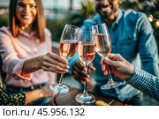 Glasses of pink sparkling wine in the hands of people. People are relaxing on the outdoor veranda. The concept of recreation, corporate event, party or celebration. Стоковое AI-изображение, AI-художник Photojuli / Фотобанк Лори